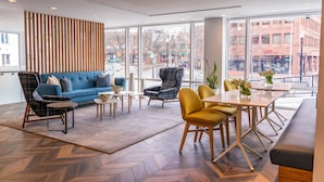 Un intérieur moderne avec un canapé bleu, des fauteuils à motifs, un mur d’accent en bois et de grandes fenêtres offrant une vue sur la ville.