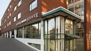 Un bâtiment en briques doté de grandes fenêtres et d’une enseigne indiquant « Harvard Hotel Square ».