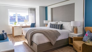 Une chambre d’hôtel moderne, dotée d’un grand lit, de tables de chevet, d’un bureau et d’une fenêtre donnant sur des immeubles.