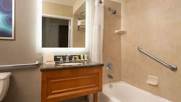 A bathroom with a wooden vanity, a sink, a mirror, a shower with a grab bar, and a toilet.