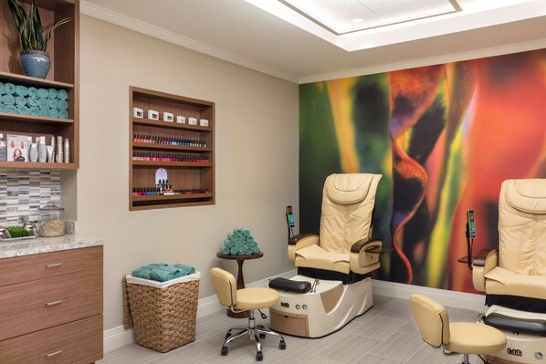 A modern spa room with a massage chair, shelves with toiletries, and a colorful abstract mural.