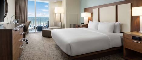 Une chambre d’hôtel avec un grand lit, un bureau, une chaise, une commode et une vue sur l’océan.