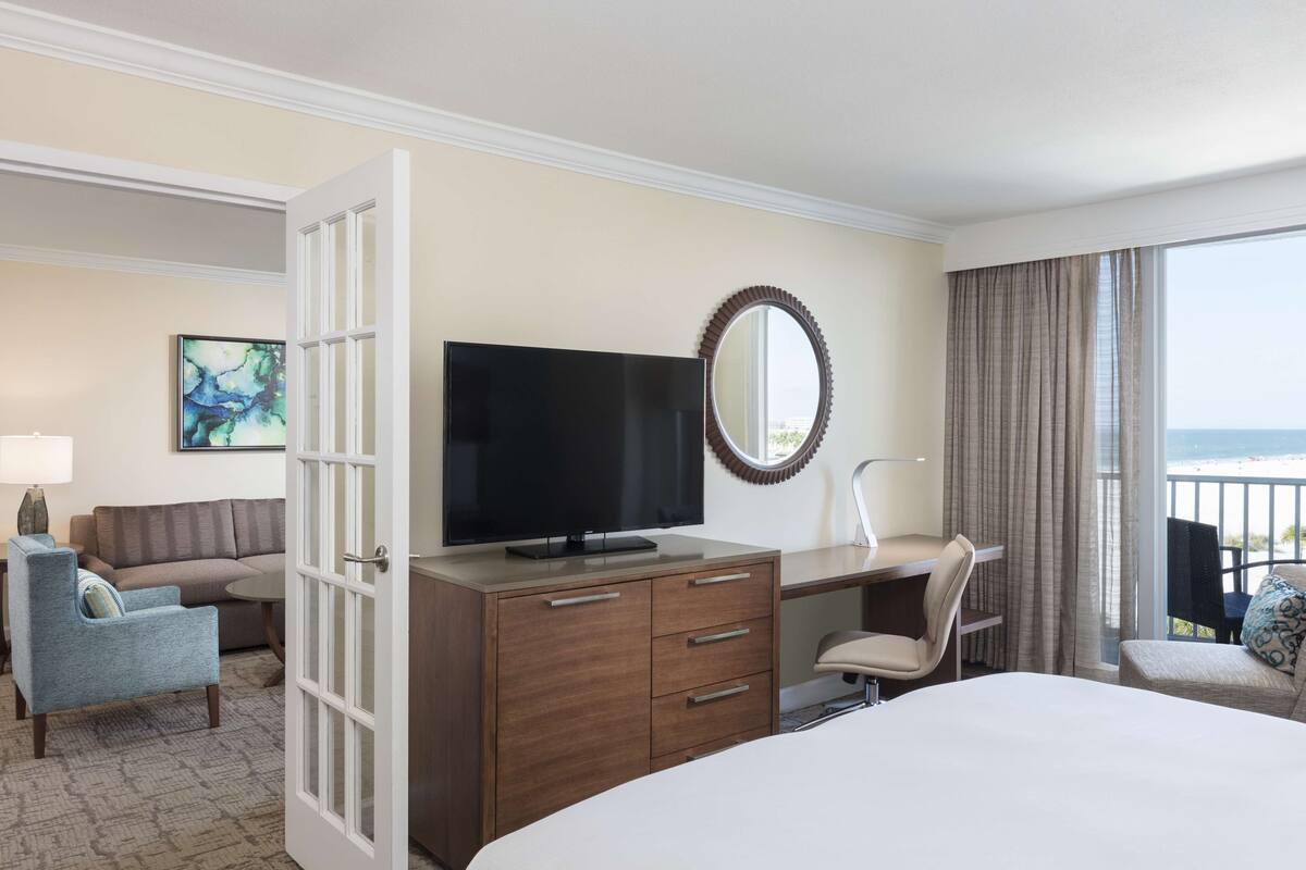 Une chambre d’hôtel équipée d’un lit, d’une télévision, d’un bureau, d’une chaise, d’un canapé et offrant une vue sur l’océan.