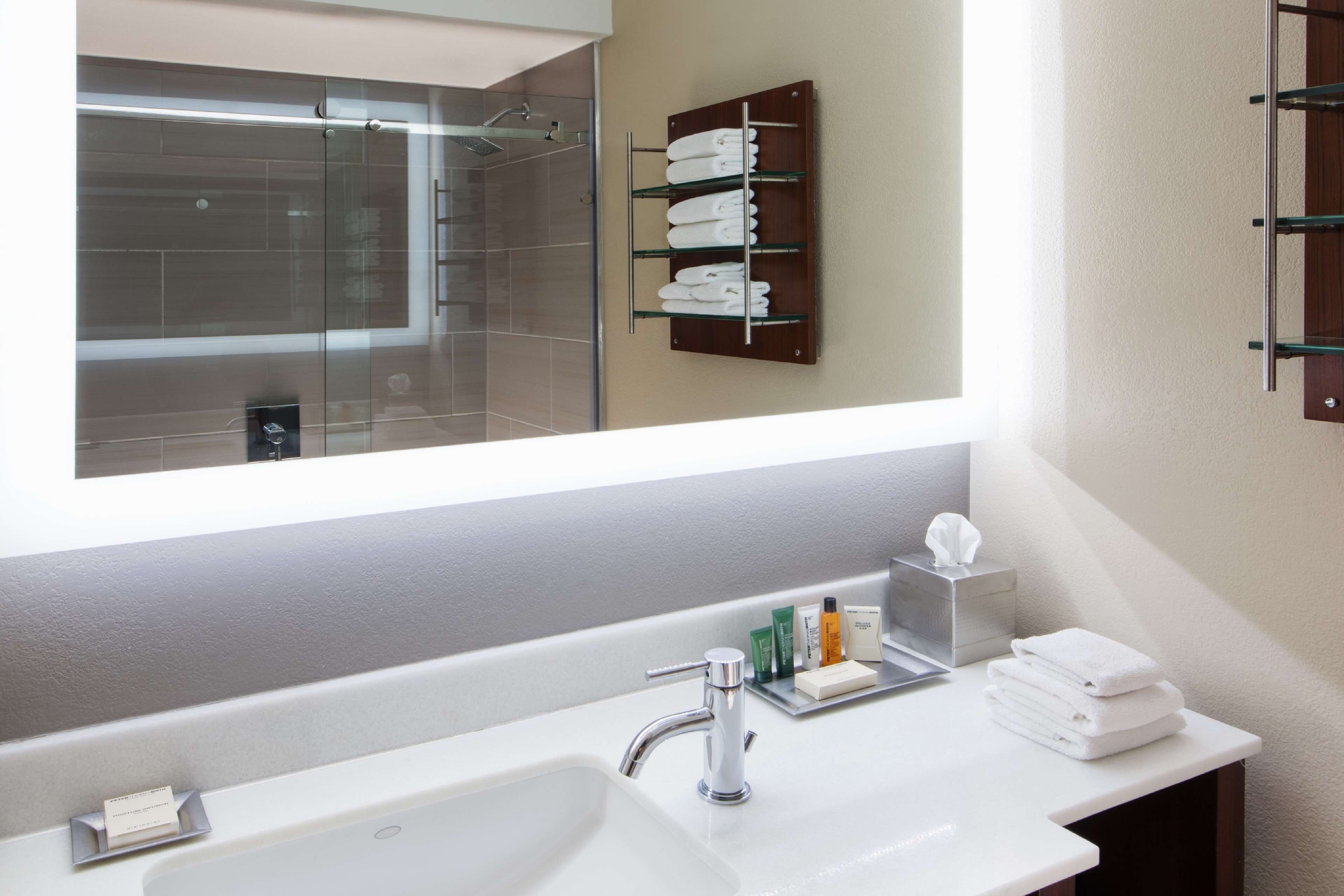 A modern bathroom with a large mirror, a white sink, and a towel rack.
