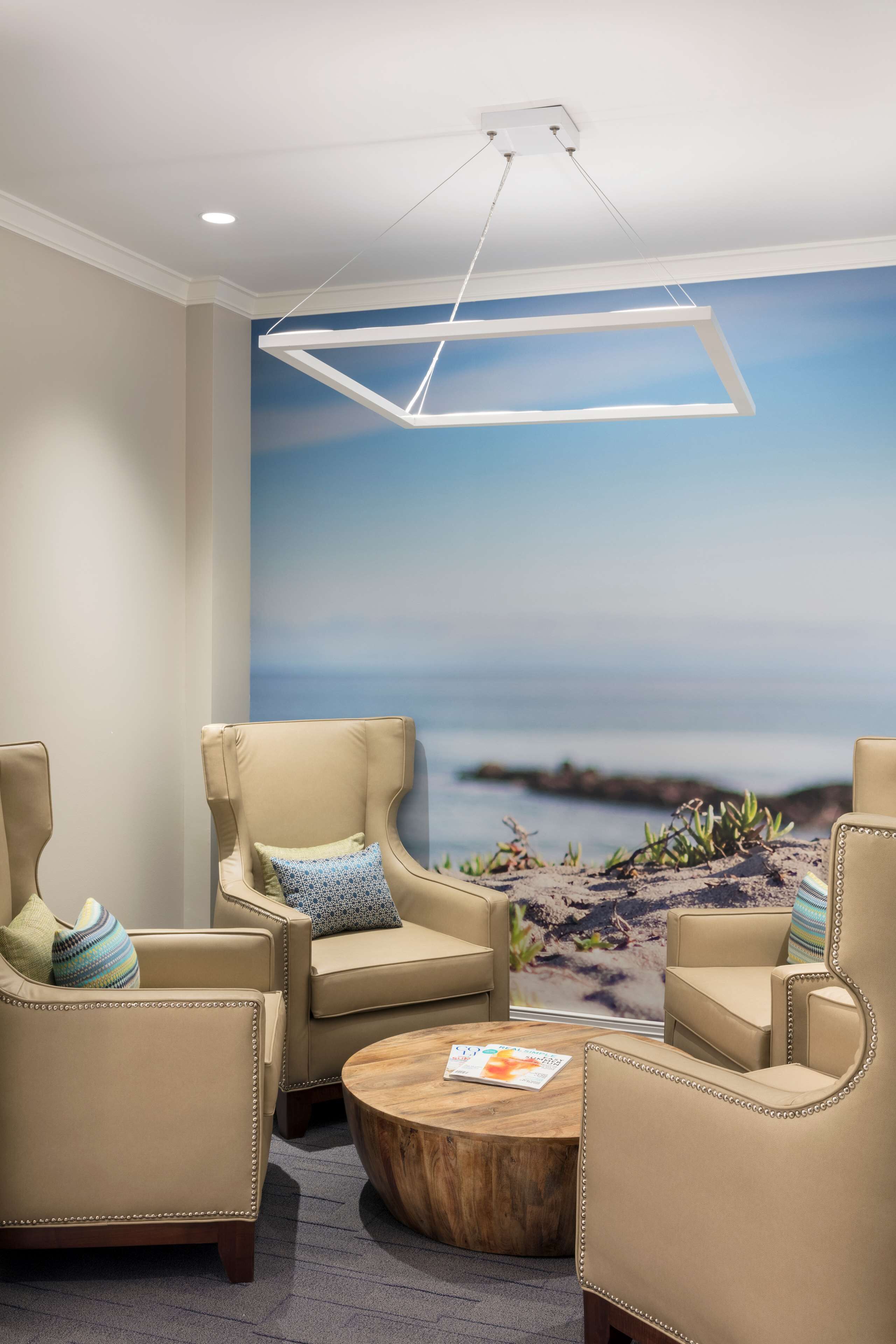A room with beige leather chairs, a wooden coffee table, and a mural of a beach scene.