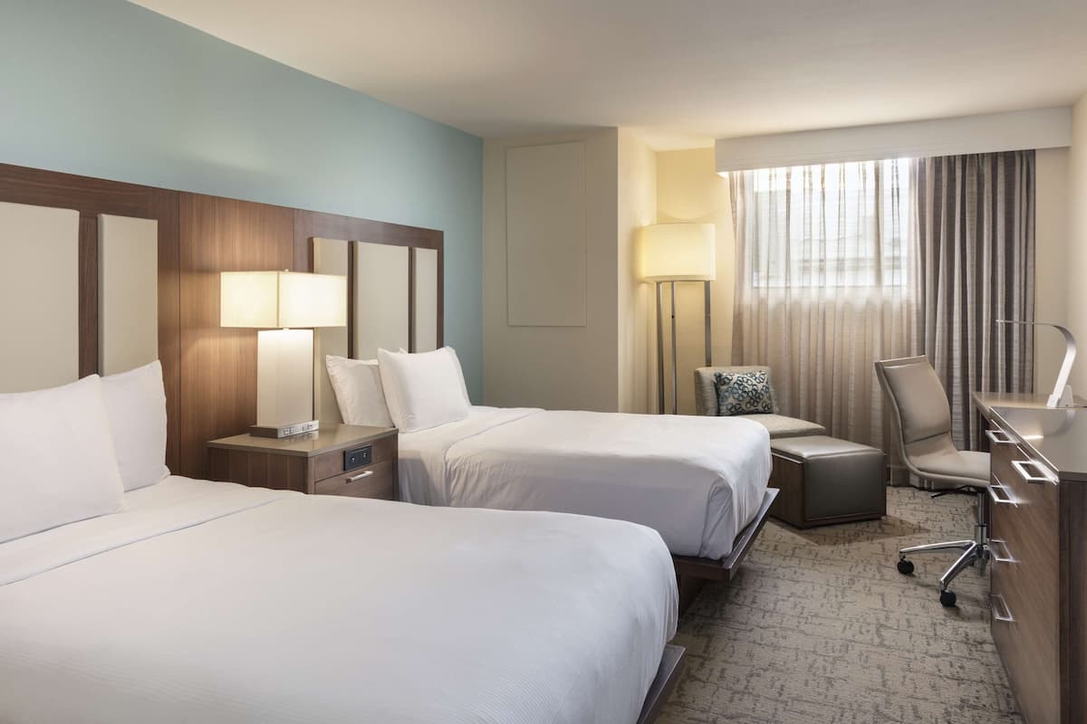 Une chambre d’hôtel avec deux lits, un bureau, une chaise et une lampe.