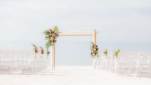 Une cérémonie de mariage organisée sur la plage, avec une arche en bois et des chaises blanches.