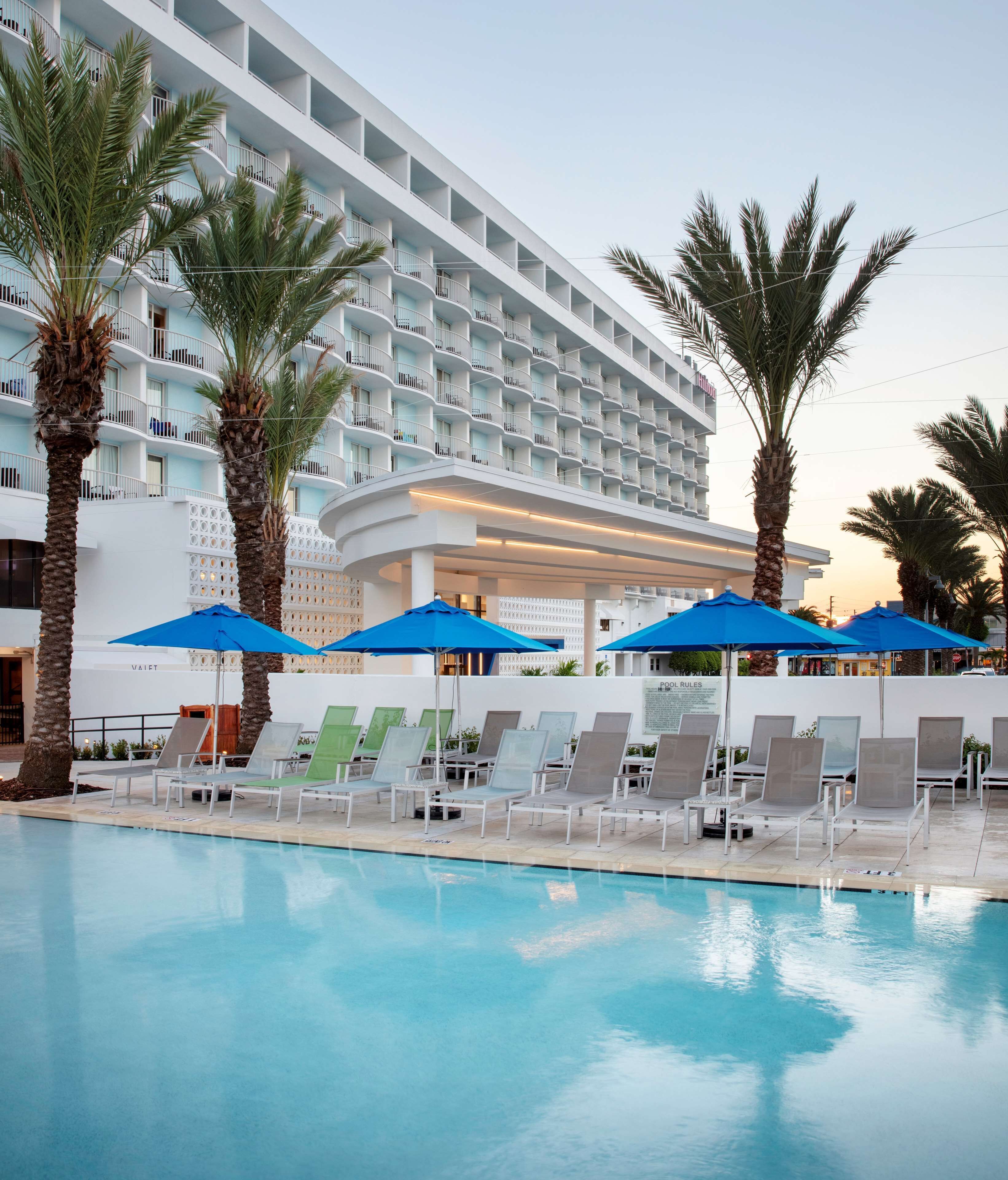 A hotel with a pool area, sun loungers, and palm trees.