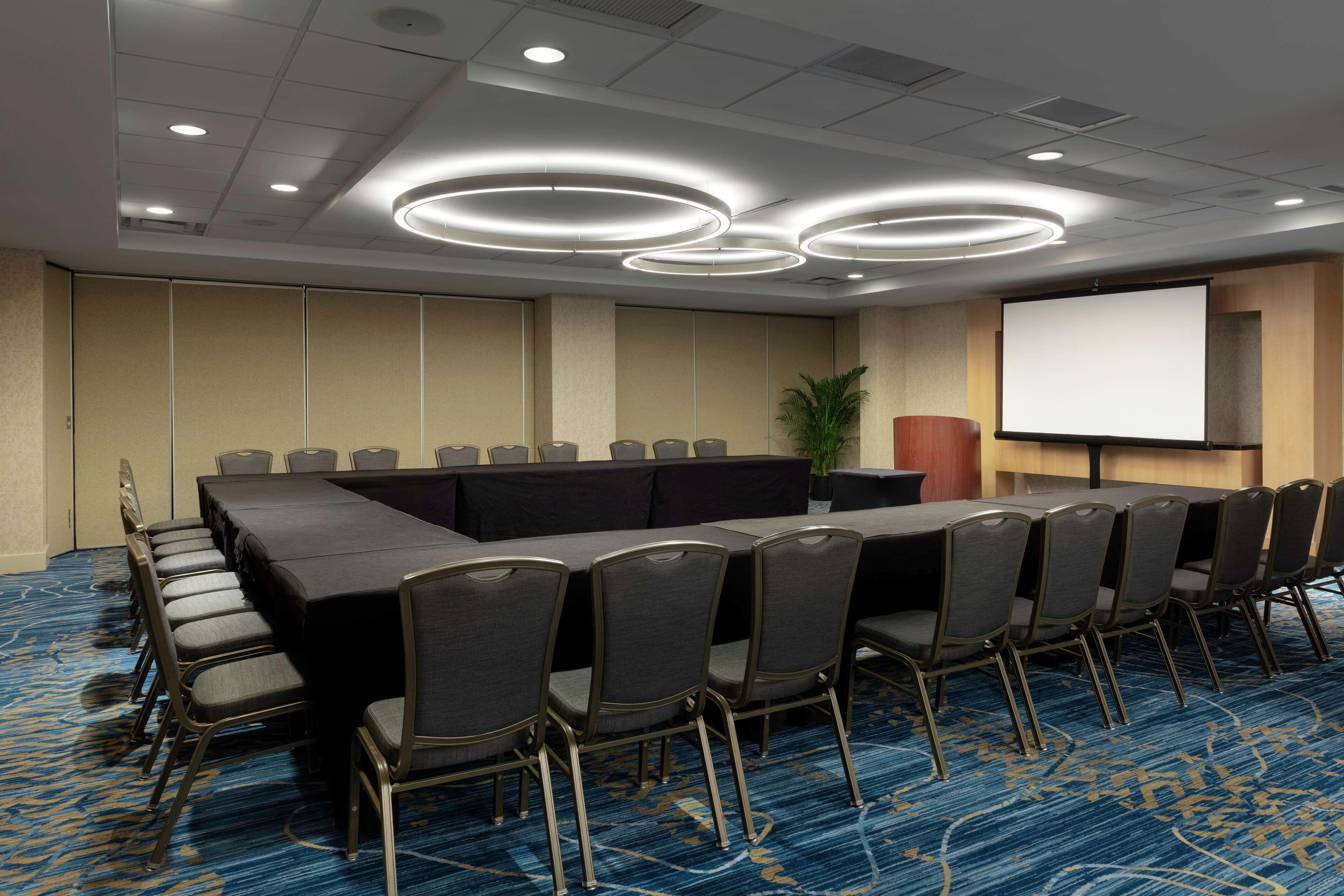 A conference room with a long table, chairs, a projector screen, and a carpeted floor.