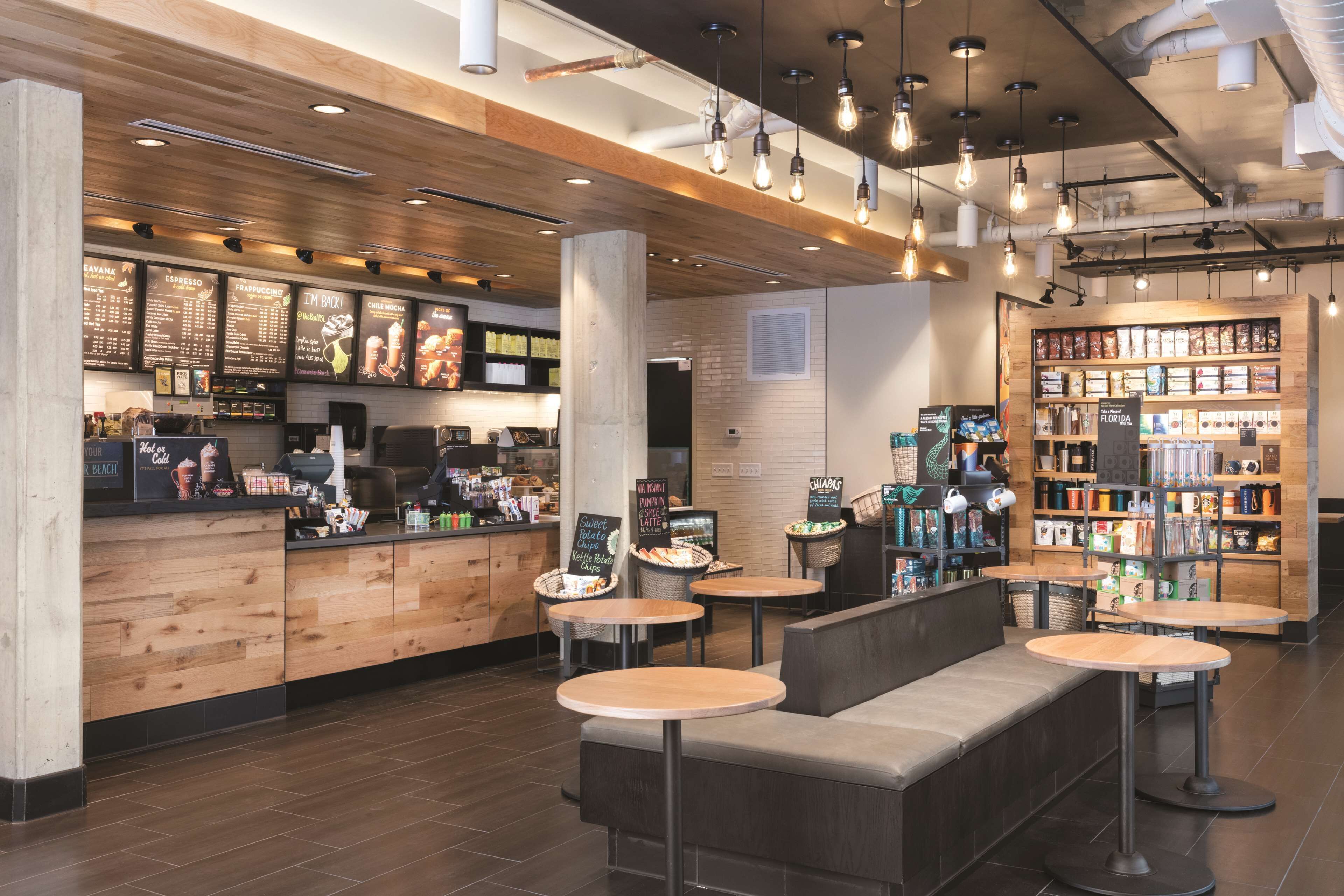 A modern cafe interior with a wooden counter, seating area, and a variety of food and drink options.