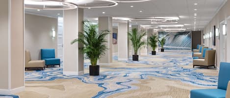 A modern hotel lobby with a patterned carpet, seating areas, and potted plants.