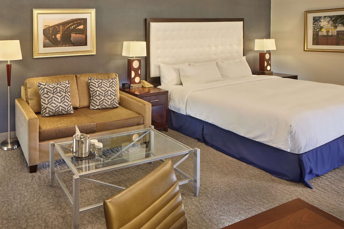 A hotel room with a bed, a sofa, a glass coffee table, and two lamps.