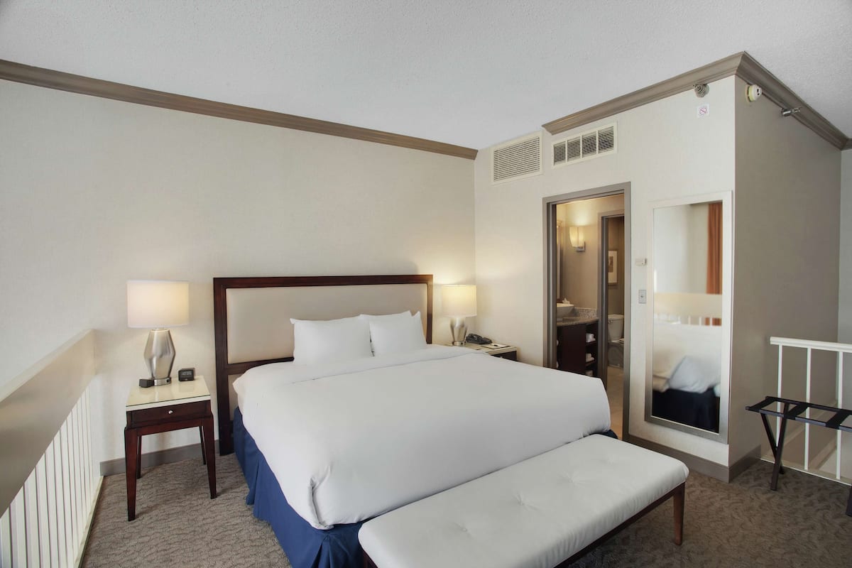 A hotel room with a large bed, bedside tables, a mirror, and a small bench.