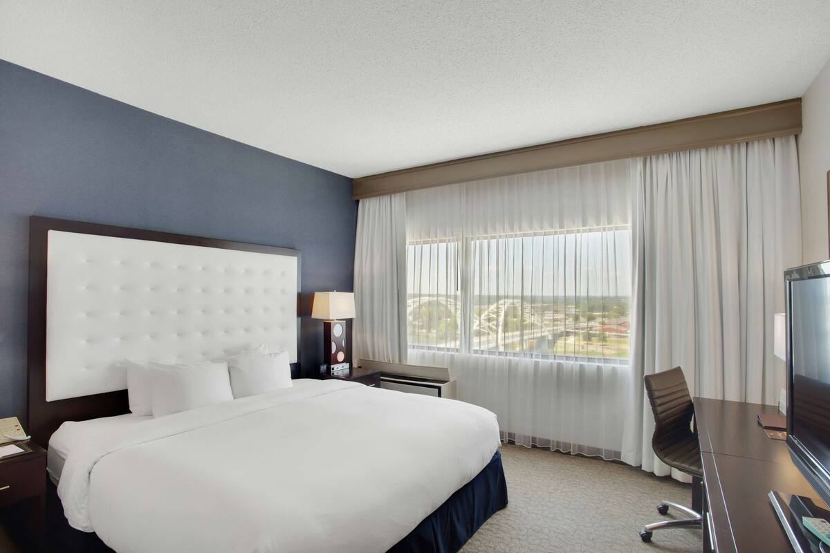 A hotel room with a large bed, a desk with a chair, a television, and a window with curtains.