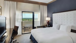 Une chambre d’hôtel avec un grand lit, un bureau avec un ordinateur, une chaise, une petite table et une vue sur l’extérieur grâce à une porte coulissante.