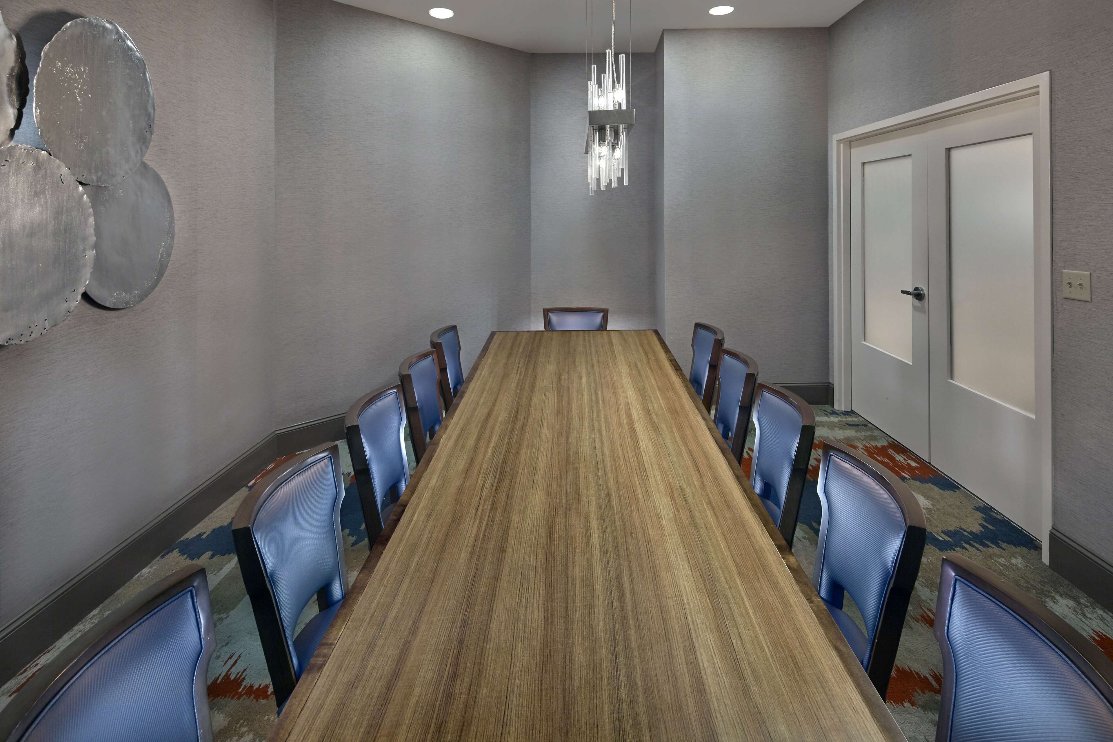 A conference room with a long table, blue chairs, a chandelier, and a door.