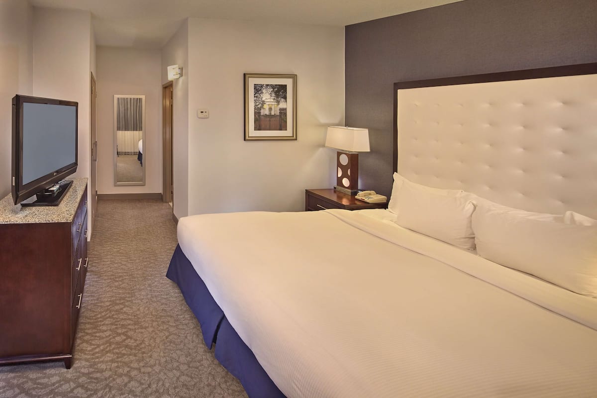 A hotel room with a large bed, a television on a dresser, a nightstand with a lamp, and a framed picture on the wall.
