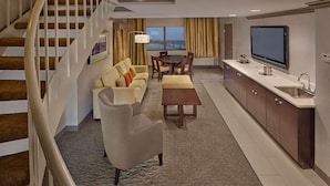 Une chambre d’hôtel moderne comprenant un coin salon, une table à manger, un canapé, une table basse, un téléviseur et un coin cuisine avec un évier et des placards.