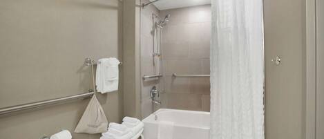 A modern bathroom with a bathtub, shower, and toilet paper dispenser.