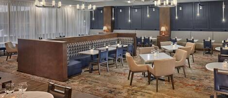 Un hall d’hôtel moderne avec un bar central, des espaces aménagés pour s’asseoir et un tapis à motifs.