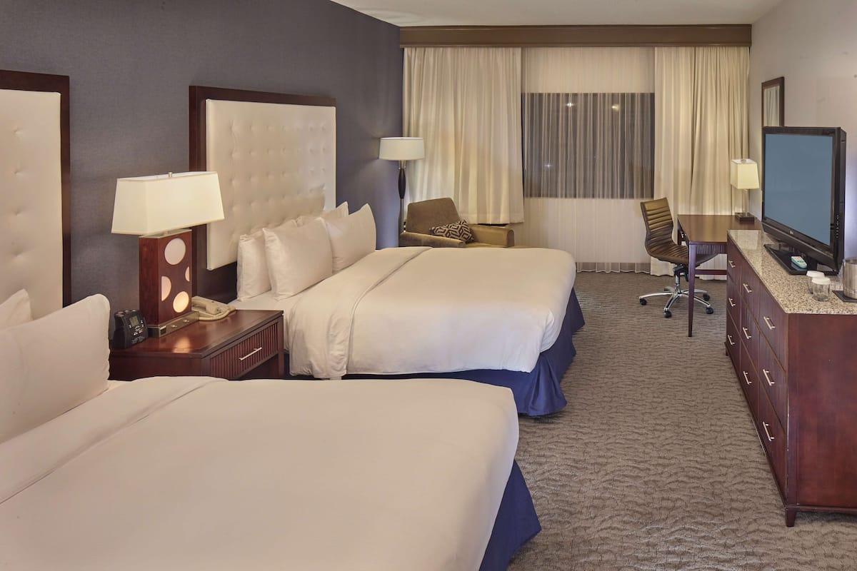 A hotel room with two beds, a desk, a television, and a chair.
