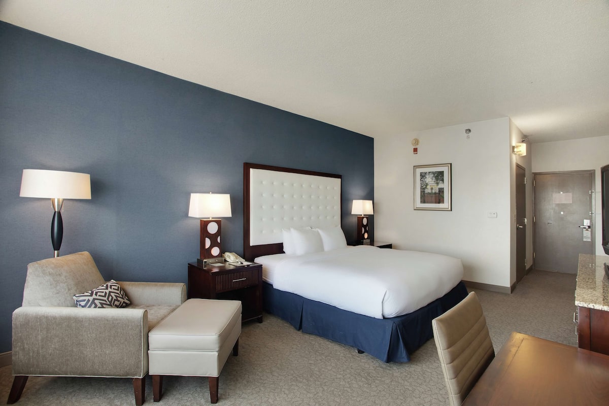 A hotel room with a large bed, a chair, a desk, and a nightstand with lamps.