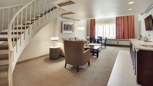 Un vaste espace de vie comprenant un escalier en colimaçon, un fauteuil confortable, une table à manger et un coin cuisine avec un évier.
