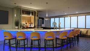 A modern bar area with a long counter, multiple stools, and a large window providing a view. - The Westin Tysons Corner (Falls Church)
