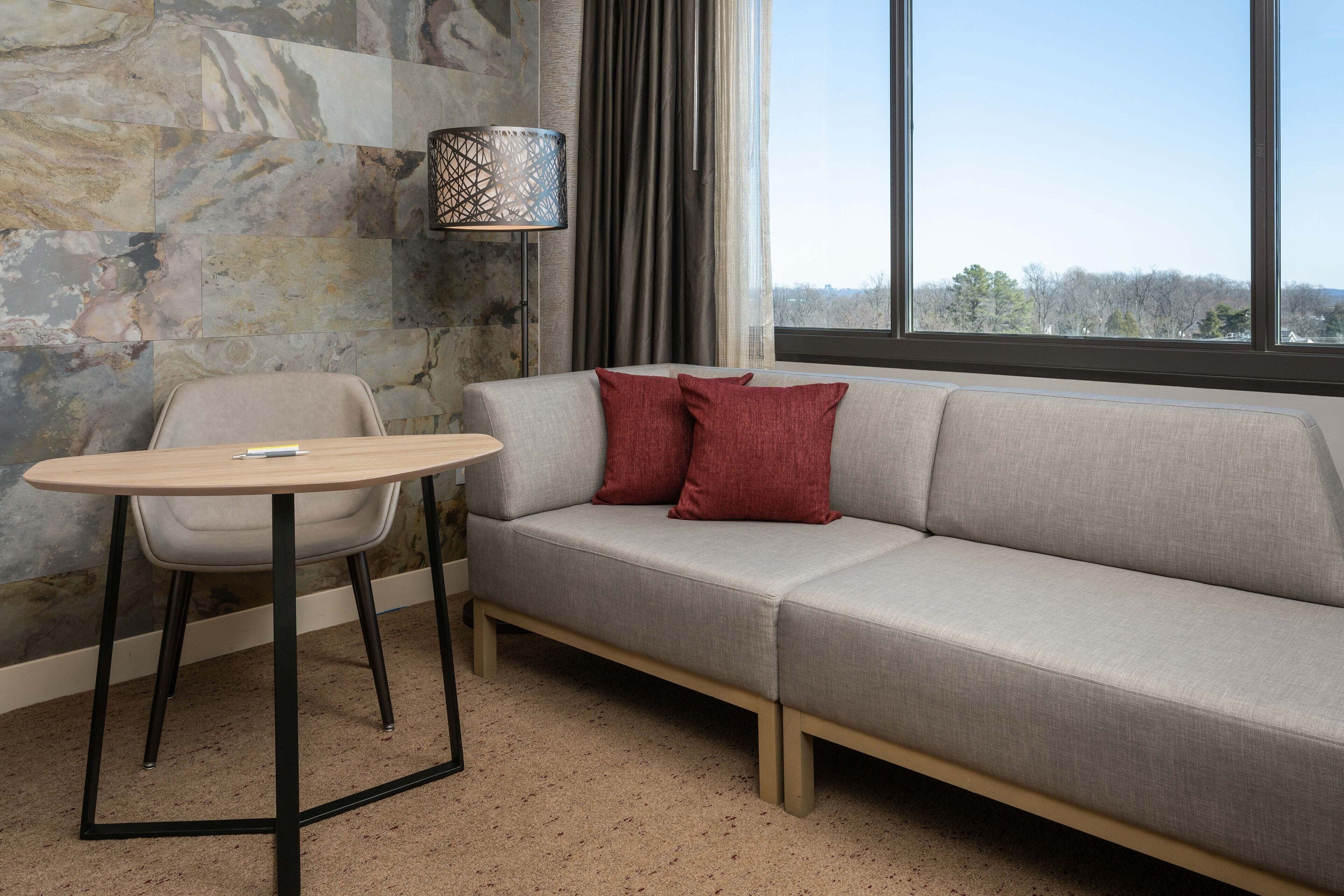 A modern living room with a grey sofa, red cushions, a round table, and a lamp.