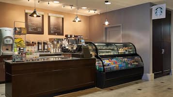 A coffee shop interior with a counter, coffee machines, a display case with snacks, and hanging lights.
