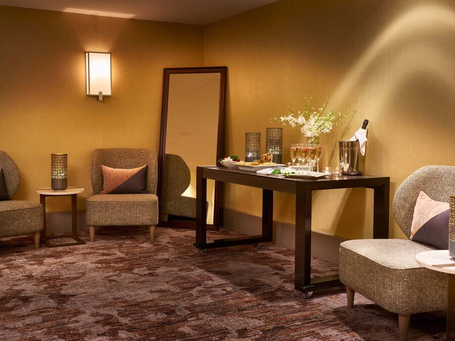 A room with two armchairs, a small table with a bottle and glasses, a large mirror, and a decorative vase.