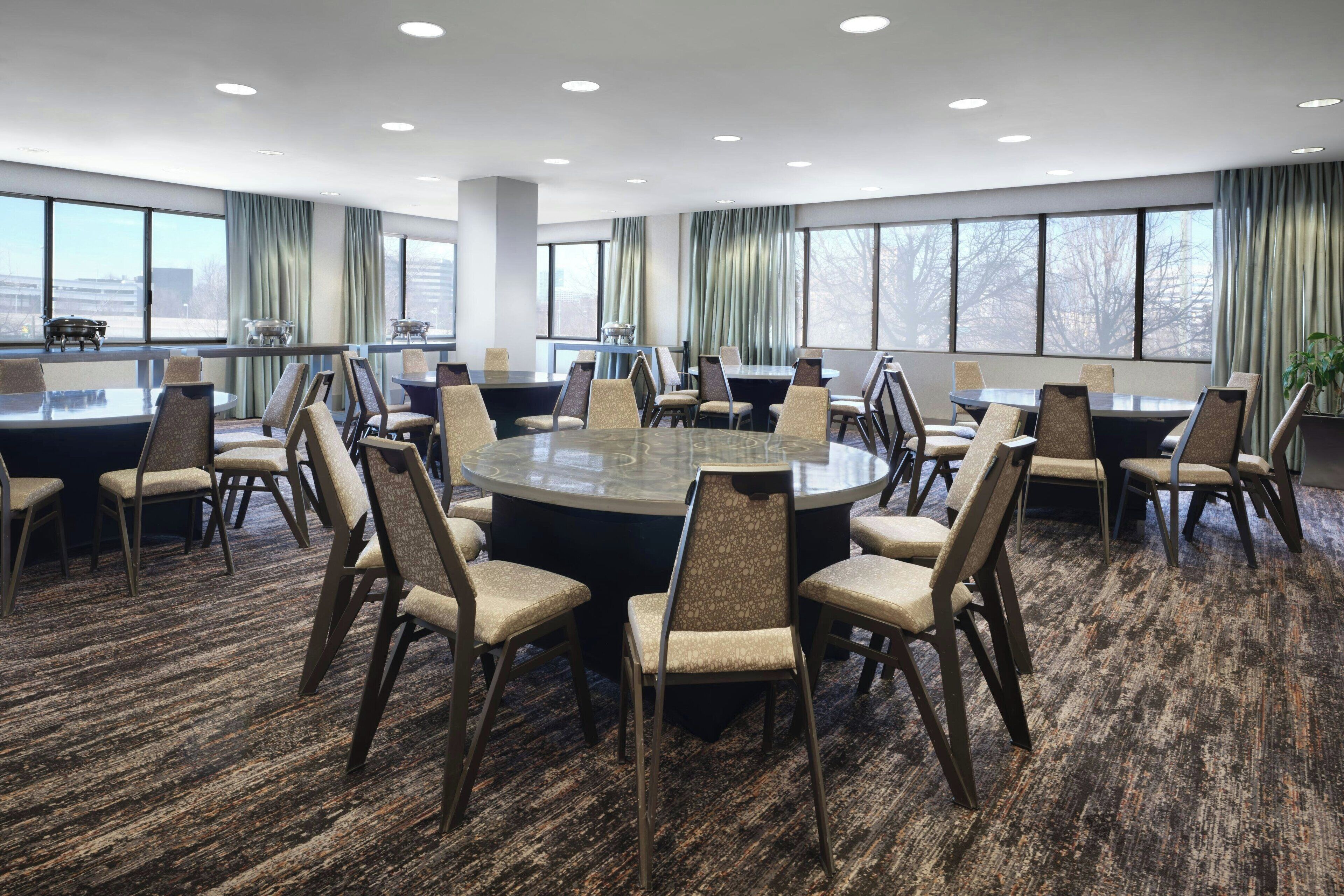 A conference room with a round table, multiple chairs, and large windows with curtains.