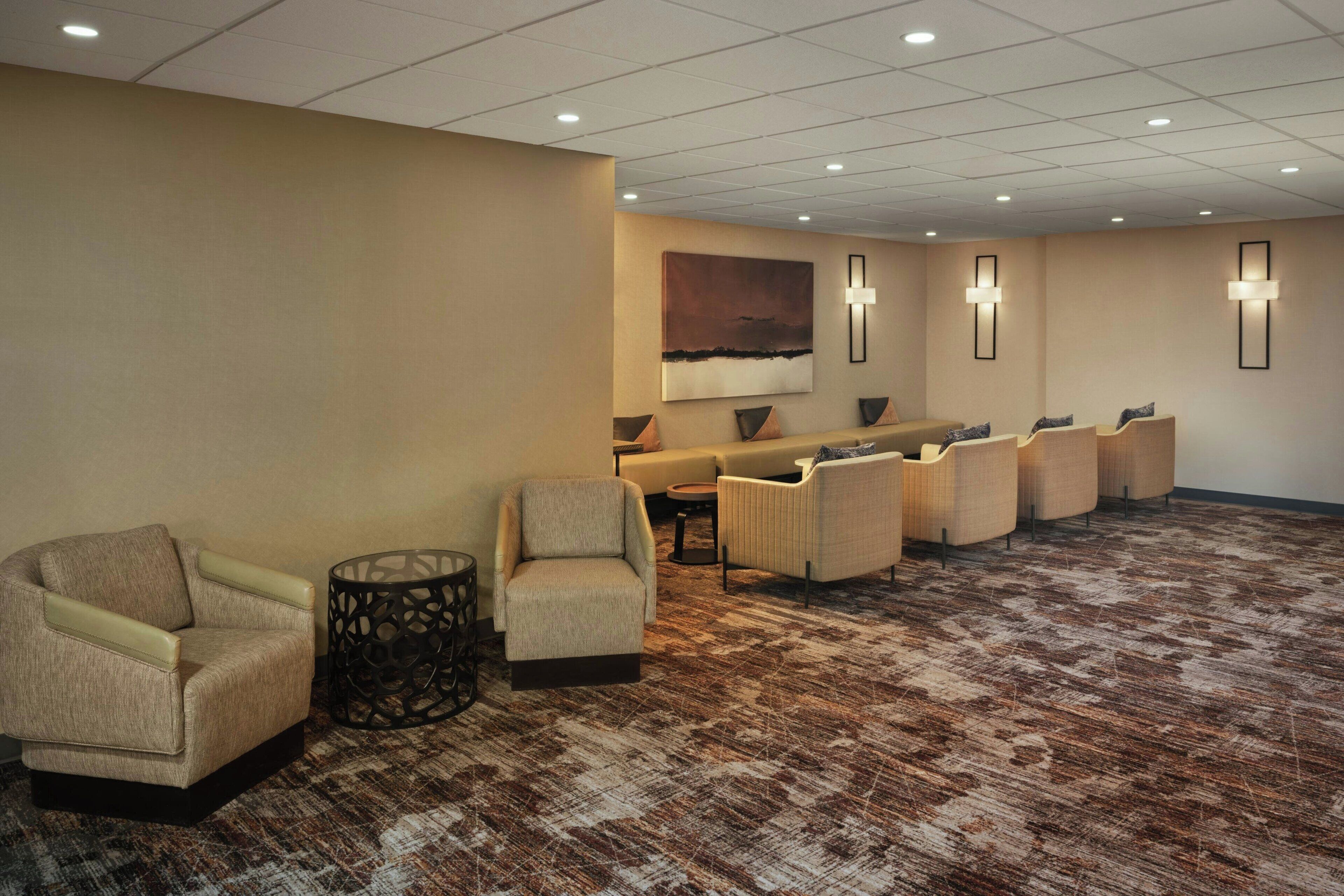 A hotel lobby with a carpeted floor, several sofas, a small table, and wall-mounted lights.