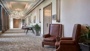 Un vestíbulo de hotel con un largo pasillo, sillones de cuero, un mostrador de recepción y una araña.