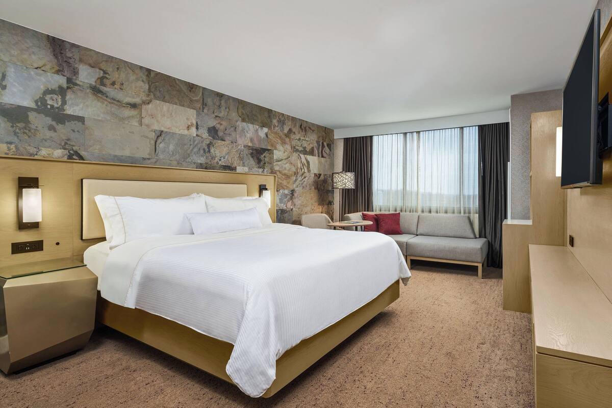 A hotel room with a large bed, a sofa, a TV, and a stone wall.