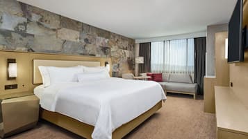 Habitació d'hotel amb un llit gran, un sofà, una televisió i una paret de pedra.
