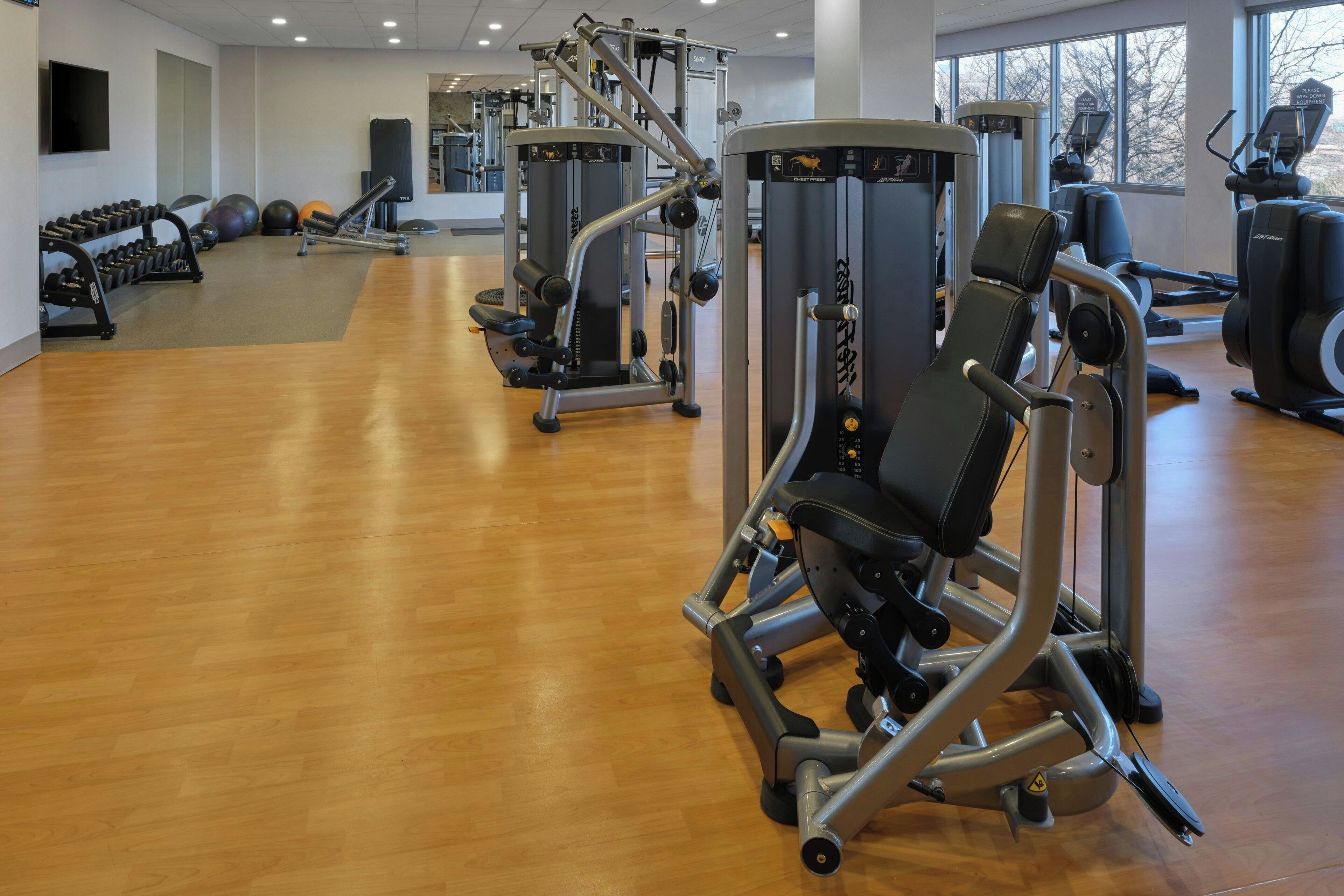 A gym with various exercise machines, a mirror, and a wooden floor.