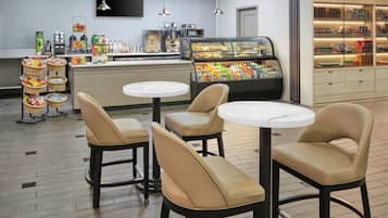 A cafe with three round tables and chairs, a coffee machine, and a display case with snacks.