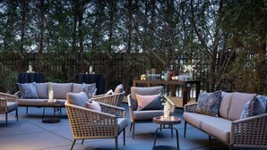 An outdoor seating area with wicker furniture, a bar, and a view of trees. - The Westin Tysons Corner (Falls Church)