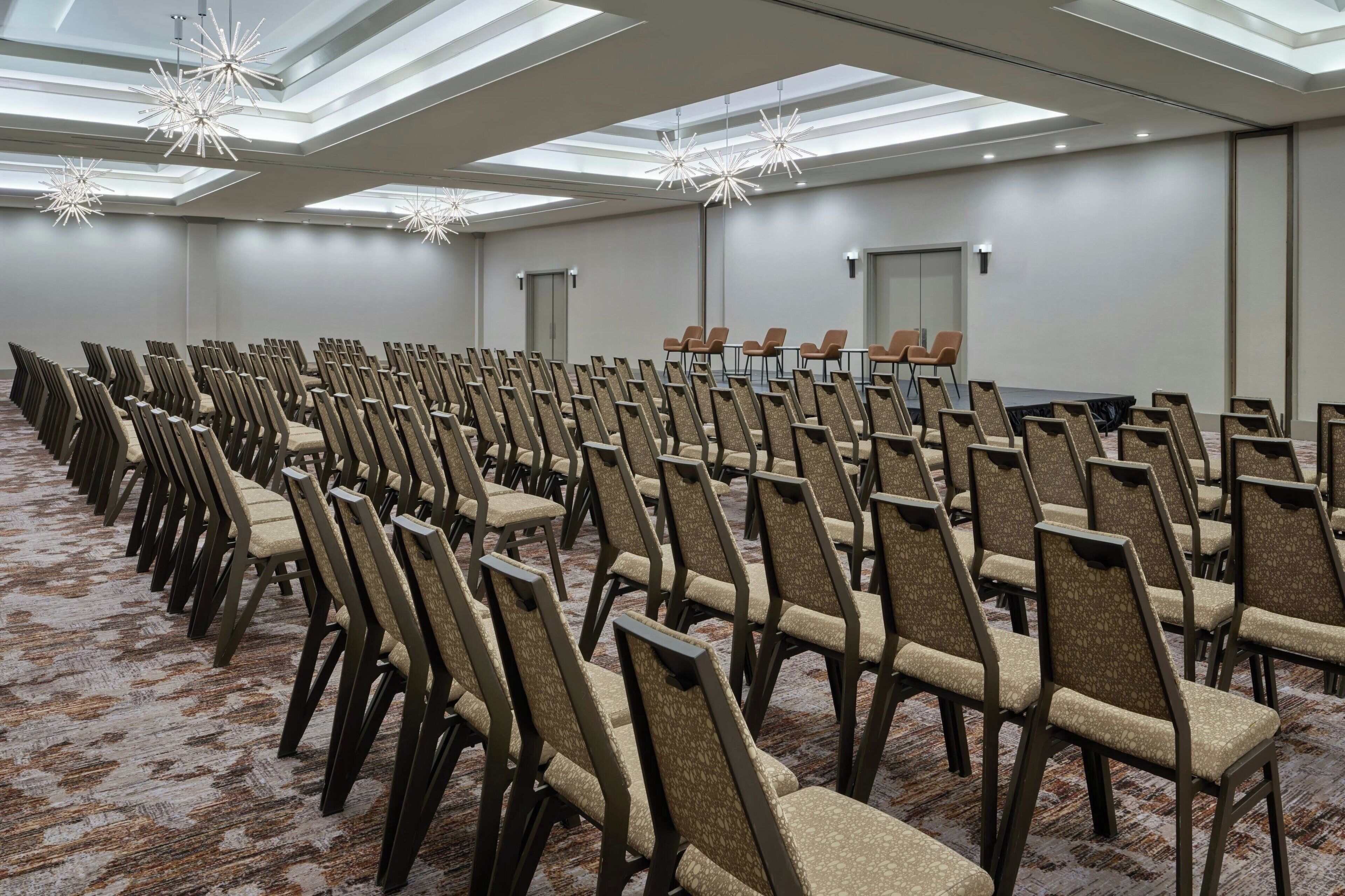 Una sala conferenze con file di sedie, un palco e un soffitto con lucernari.