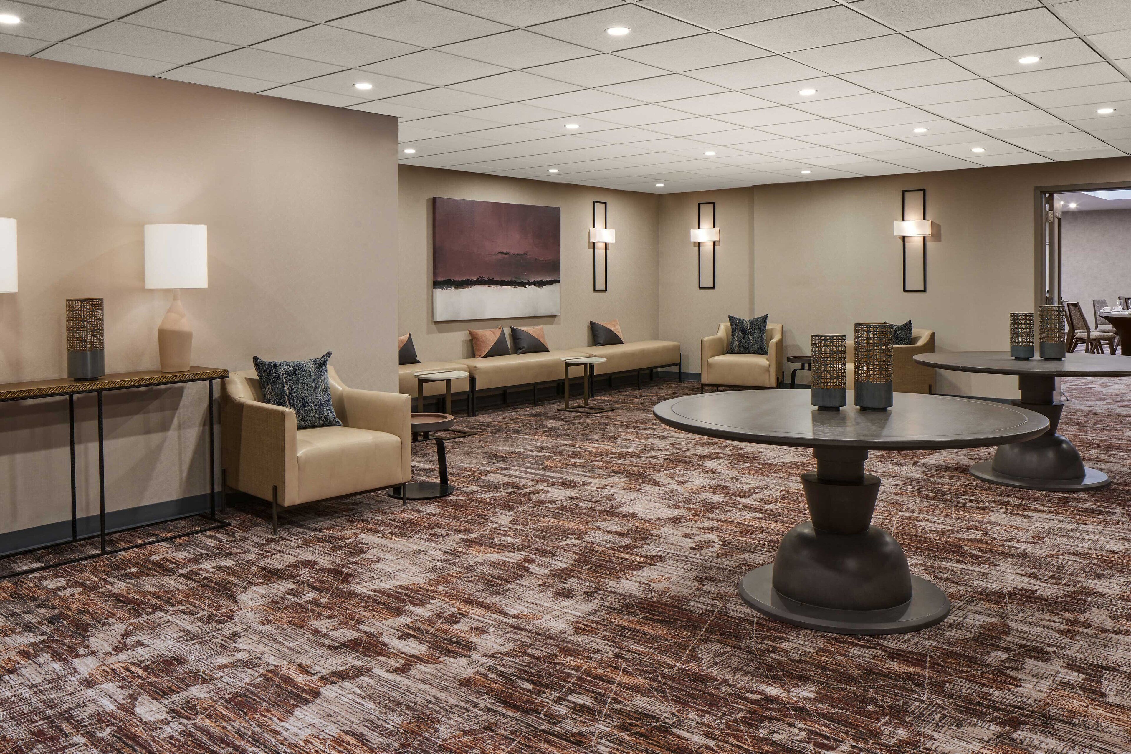A hotel lobby with sofas, tables, and a large painting on the wall.