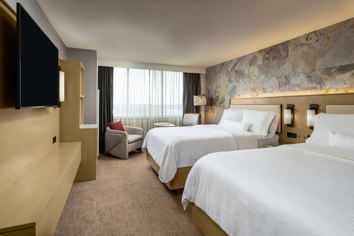 A hotel room with two beds, a TV, a sofa, and a large window with curtains.