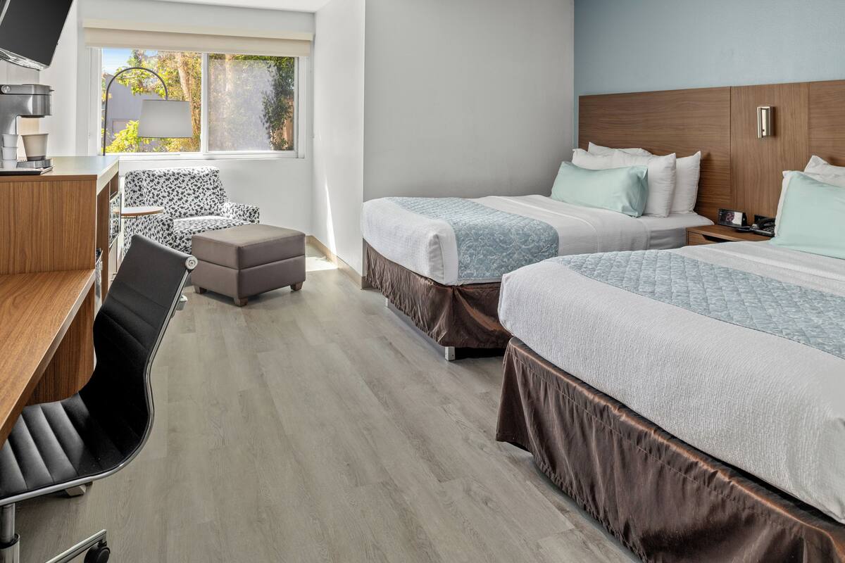 Habitación de hotel con dos camas, un escritorio, una silla y una ventana que da a árboles.