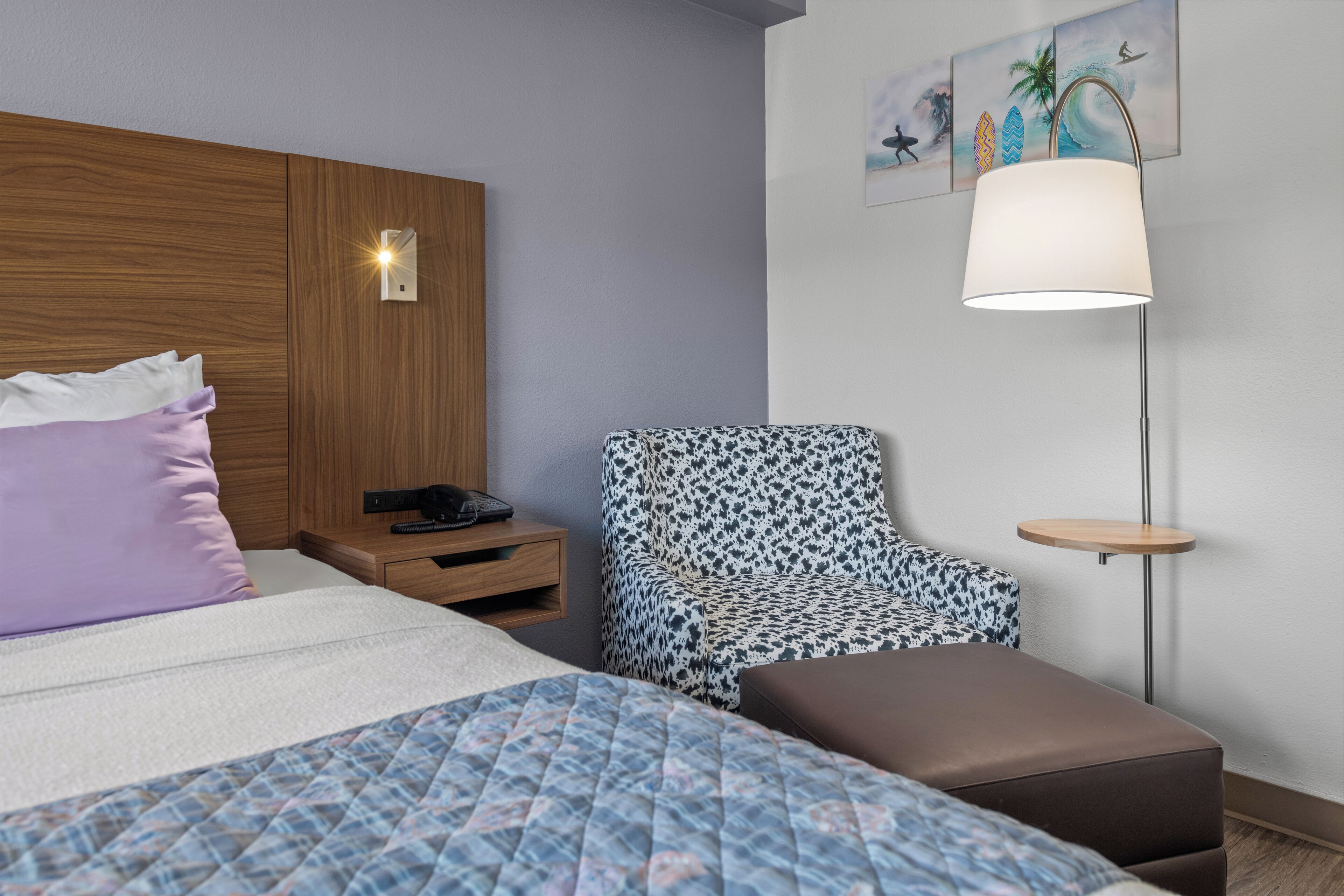Una habitación de hotel con una cama, un sillón estampado, una mesita y una lámpara de pared.