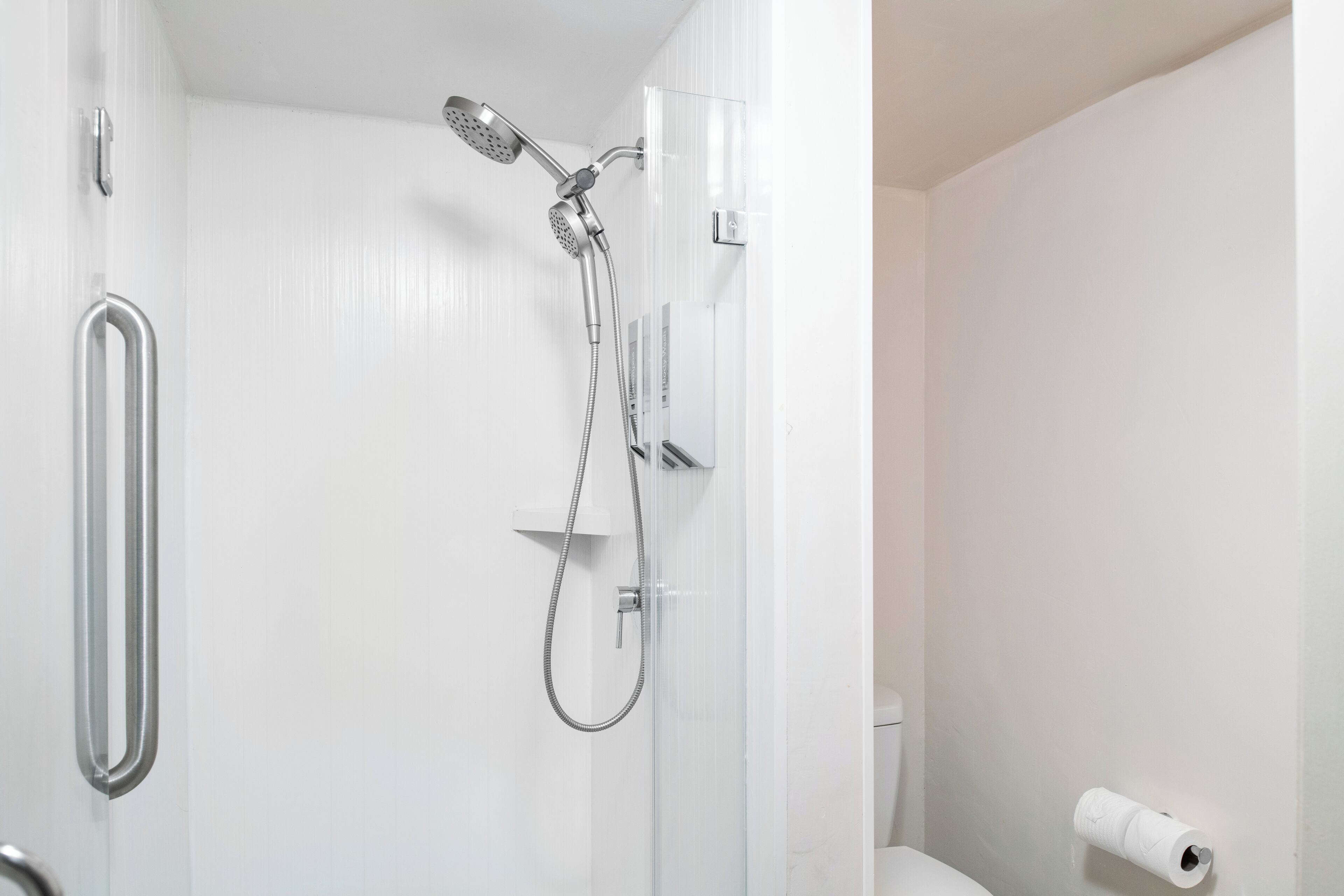 Un baño con ducha, inodoro y soporte para papel higiénico.