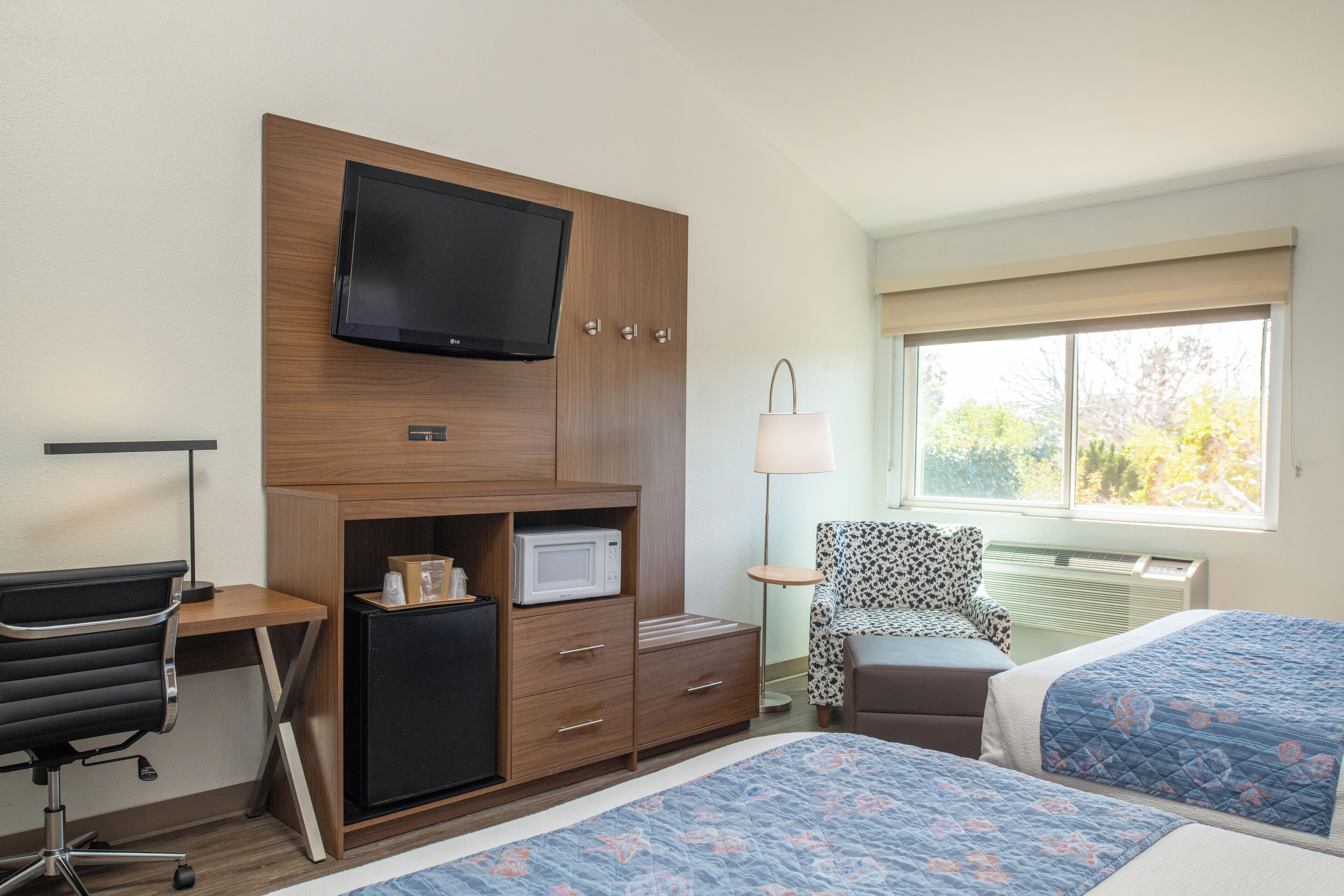 Una habitación de hotel con cama, escritorio, computadora, televisor, microondas y una silla.