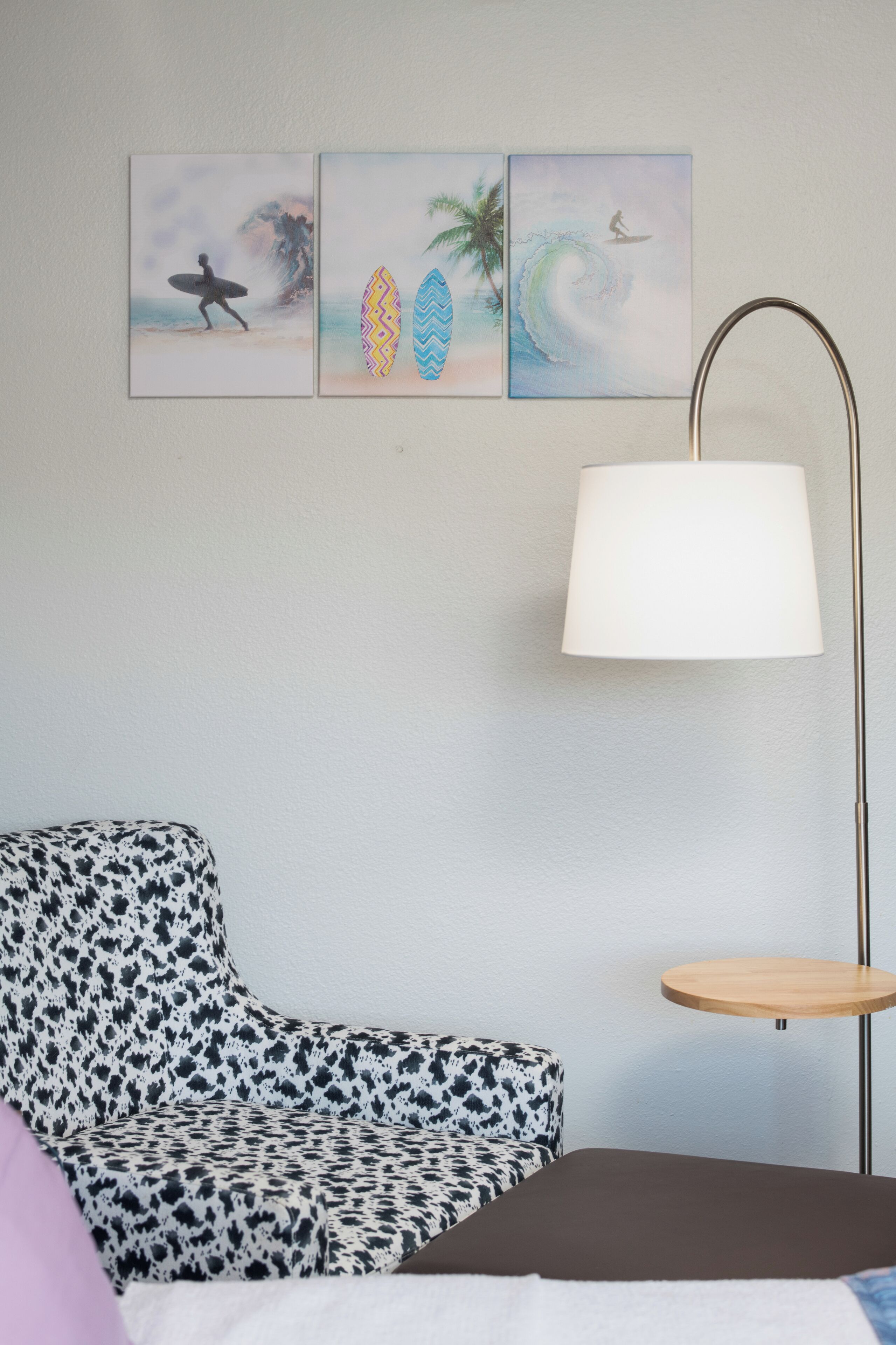 A room with a patterned sofa, a small table, and wall art depicting surfers and waves.