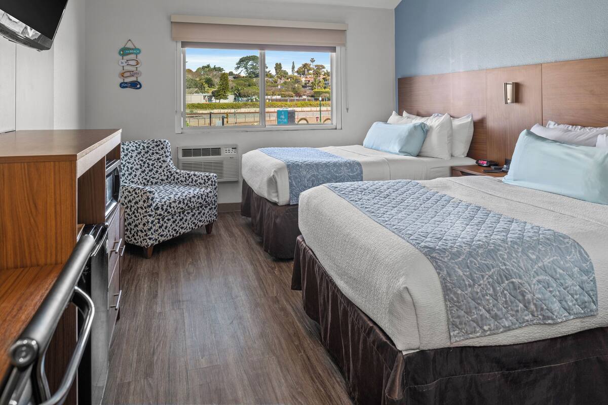 Habitación de hotel con dos camas, un sofá, una silla, un televisor y una ventana con vista a un parque.