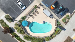 Vista aérea de un estacionamiento con piscina, rodeado de vegetación y con sombrillas.