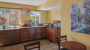 Una cocina con armarios de madera, una mesa de comedor y sillas. Se ve una ventana con vistas al exterior.